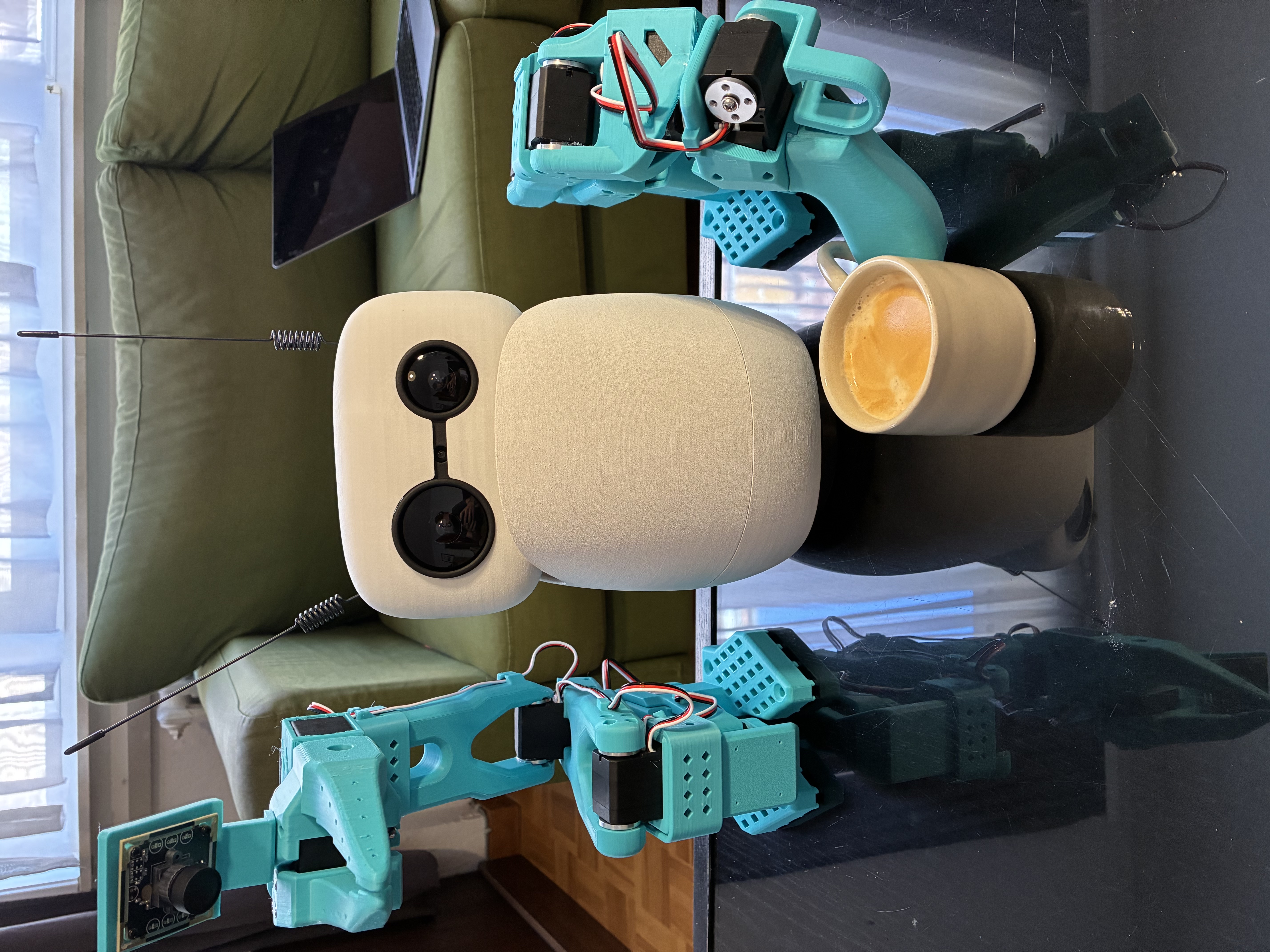 Reachy Mini with SO-101 arms on a table, one arm holding a cup of coffee